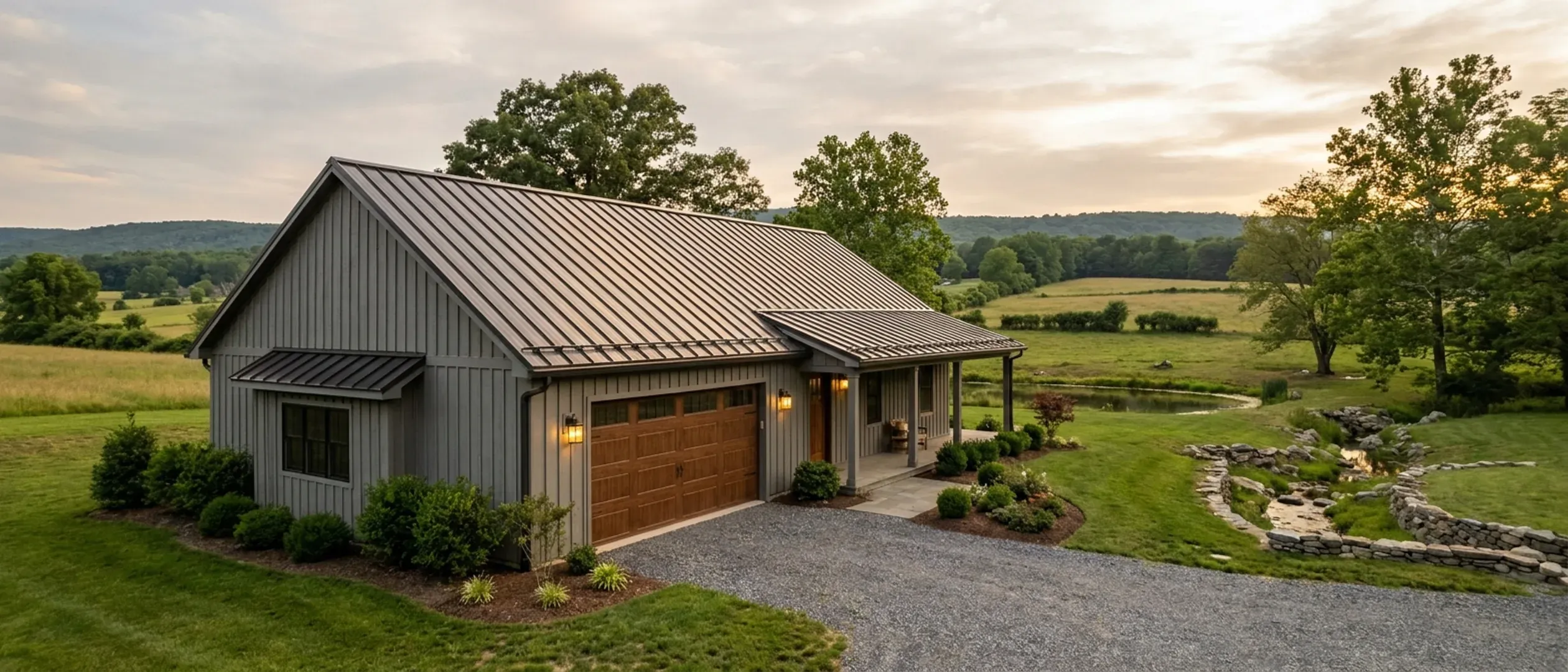 A completed barndominium viewed from a low angle showing its standing seam metal roof, vertical wall panels, gutters and exterior wall lights.