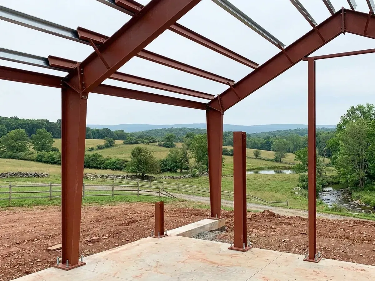 A red oxide primed structural steel frame partly erected on a concrete slab, showing bolted knee joints and anchor bolts.
